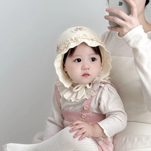 Detail of knitted baby hat with lace trim and floral accents in a soft cream color