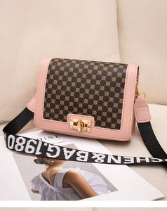 Detail of pink and brown monogram crossbody bag with wide strap on a sofa