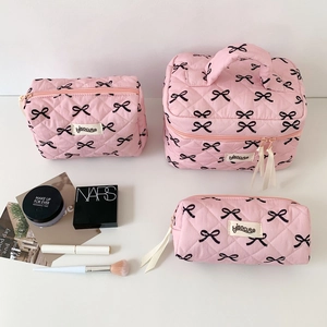 Detailed set of pink quilted makeup bags featuring black bow prints and ribbon zippers