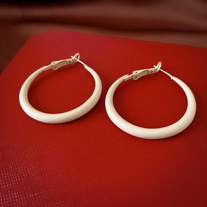 Detail view of large cream hoop earrings with smooth matte finish on dark red base