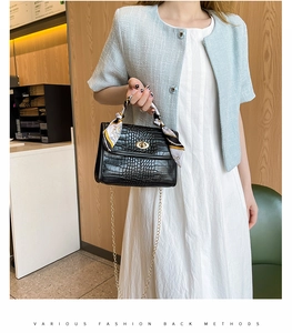 Detail of black crocodile texture bag with gold chain strap and silk scarf wrapped handle