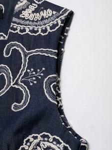 Detailed macro view of white embroidery patterns on dark blue denim fabric texture