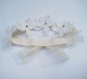 Dettaglio macro della giarrettiera da sposa in pizzo bianco con strass e fiori applicati