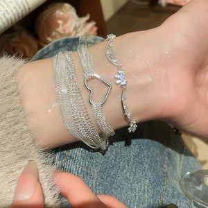 Detail of layered silver heart bracelet with zircon flowers on a woman's wrist