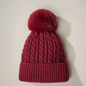 Dark red cable knit beanie featuring a fluffy pompom and thick ribbed cuff for warmth