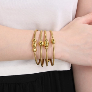 Detail showing a stack of four twisted gold cable wire bracelets with metallic beads