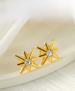 Detailed close-up of gold eight-pointed star earrings with sparkling zircon centers