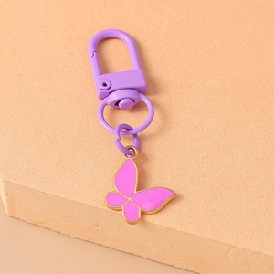 Detail of purple butterfly keychain with gold edges and metallic spring clasp on textured surface