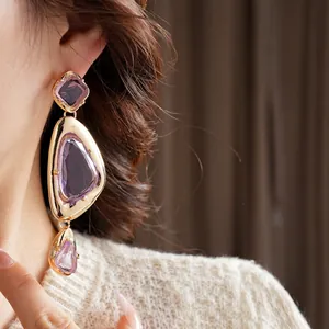 Vintage irregular gold-rimmed earrings with purple teardrop crystals on female model