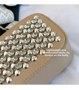 Close-up of beige leather bag featuring dense silver rhinestone studs and woven strap