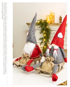Christmas gnome dolls in red and grey sitting on a wooden sleigh by a warm fireplace