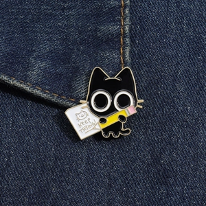 Detail of cartoon black cat enamel pin with Keep Trying text on denim fabric