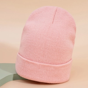 Gros plan d'un bonnet en tricot rose avec texture côtelée et large revers sur fond chaud