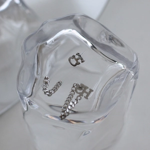 Detailed close-up of CH letter earrings with fringe chains on textured glass base