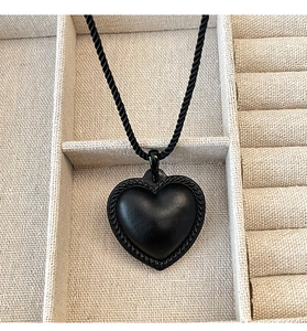Détail d'un pendentif cœur noir avec bordure tressée sur une chaîne corde dans son écrin