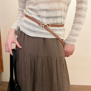 Close-up of brown leather belt featuring a golden bow buckle on a beige knit dress