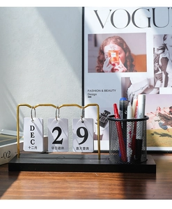Close-up of golden metal pen holder with manual flip calendar and black wooden base