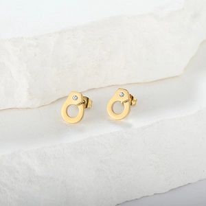 Detail of gold handcuff stud earrings with zircon stones on a white stone background