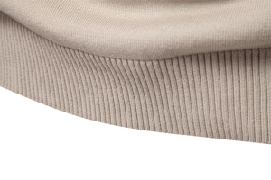 Detailed close-up of beige knitted sweater showing ribbed cuff and plain knit texture