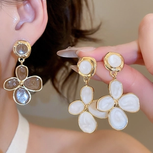 Détail de boucles d'oreilles fleurs en résine et bords dorés portées par un mannequin