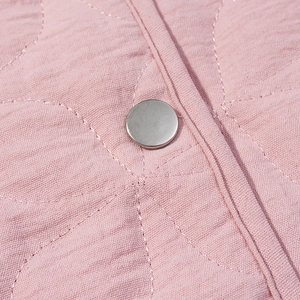 Detailed close-up of pink quilted fabric with silver metal snap button on jacket