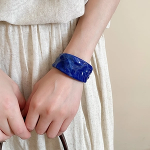 Detail of a wide blue acrylic cuff bracelet with wavy texture worn by a model