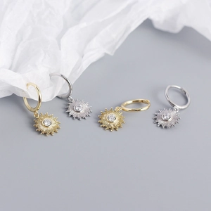 Detailed view of sun-shaped gold and silver earrings with zircon inlays