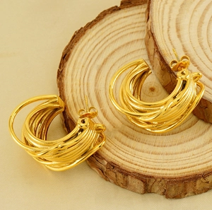 Macro shot of gold multi-layer intertwined C-shaped earrings on natural wooden slices