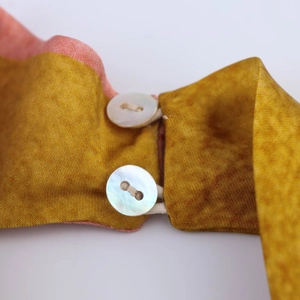 Détail du tissu en satin doré avec d'élégants boutons en nacre et boucles en cordon