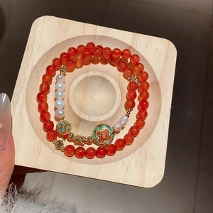 Detail of red agate and pearl beaded bracelet with a golden enamel floral pendant