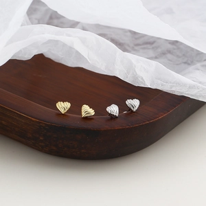 Close-up of heart-shaped textured stud earrings in gold and silver finish on wood