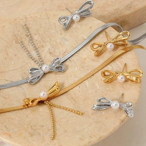 Elegant gold and silver bow pearl necklace and earring set on a marble pedestal