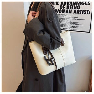 Large white leather tote bag shown on model with cute cat charm for commute