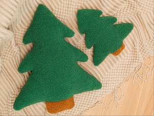 Detail of Christmas tree pillows in green sherpa fleece on a cozy beige knit blanket