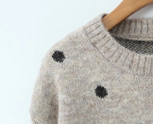 Dettaglio ravvicinato di maglione in maglia beige con scollo rotondo e motivo a pois neri