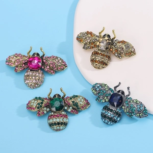 Top view of four vintage crystal bee brooches in assorted colors on a blue background