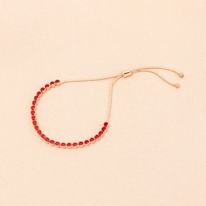 Dettaglio del bracciale tennis dorato regolabile con zirconi rossi su sfondo beige