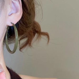 Macro shot of a dark green geometric hoop earring worn by a model in warm light
