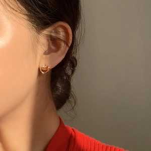 Gros plan d'une boucle d'oreille cœur doré porté par un mannequin sous lumière chaude