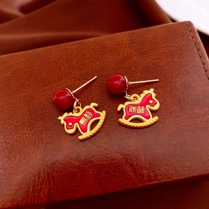 Close-up of golden rocking horse earrings with red enamel and Chinese success engraving