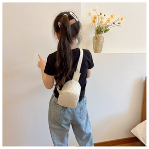 Close-up of a cream-colored minimalist kids' chest bag worn by a young model in a studio