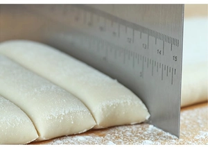 Macro shot of stainless steel dough cutter with scale measurements slicing fresh white dough