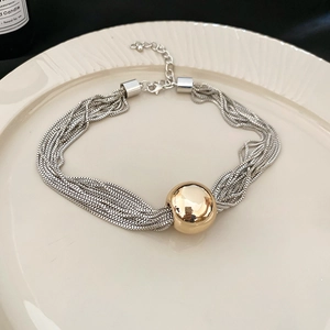 Detailed view of layered silver chains with a large golden bead on a ceramic plate