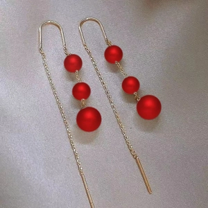 Detail of long gold chain drop earrings featuring three matte red beads on gray fabric
