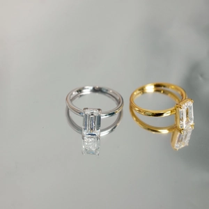 Close-up of emerald-cut zircon stones on silver and gold rings with mirror reflections