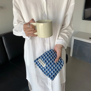 Pochette à carreaux bleue et beige tenue par un mannequin dans un intérieur chaleureux
