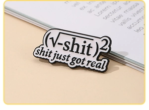 Macro detail of enamel math joke pin with "shit just got real" text on a book