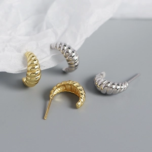Macro detail of gold and silver twisted croissant earrings with glossy metallic texture