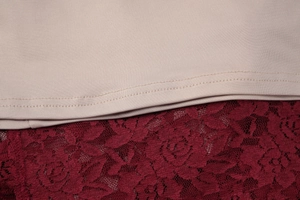 Dettaglio ravvicinato del tessuto beige cucito con pizzo floreale bordeaux e cuciture