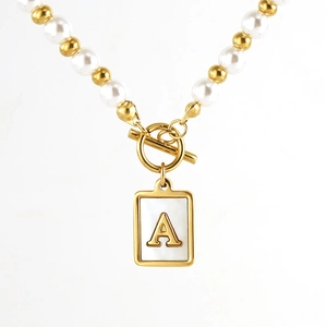 Close-up of golden necklace with pearls, T-bar clasp and letter A shell pendant
